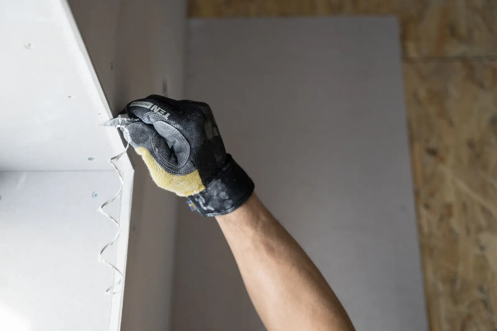 Gloved hand trimming a hung drywall panel during a wall repair