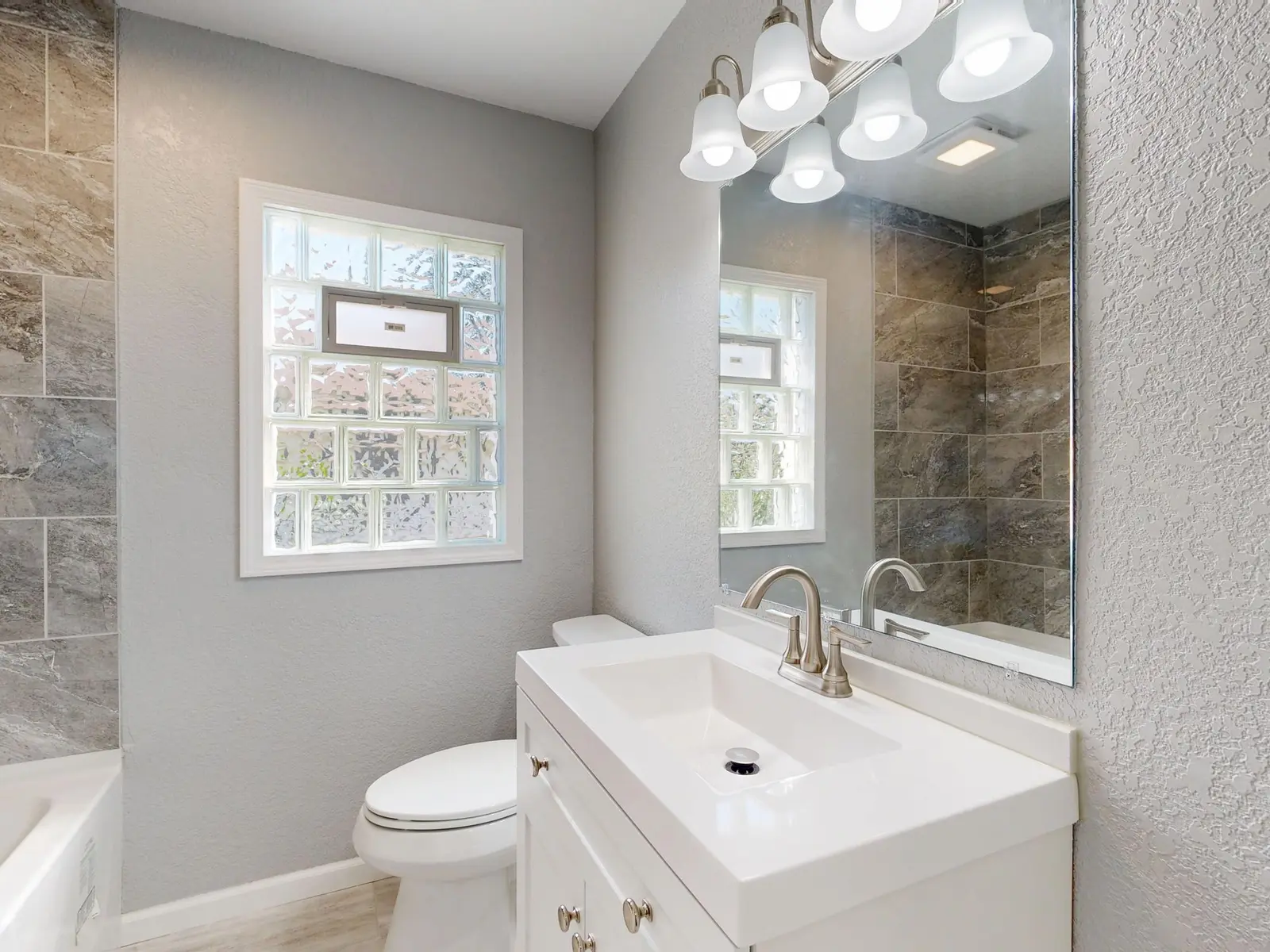 Finished bathroom with a new vanity, grey tile and a bright window