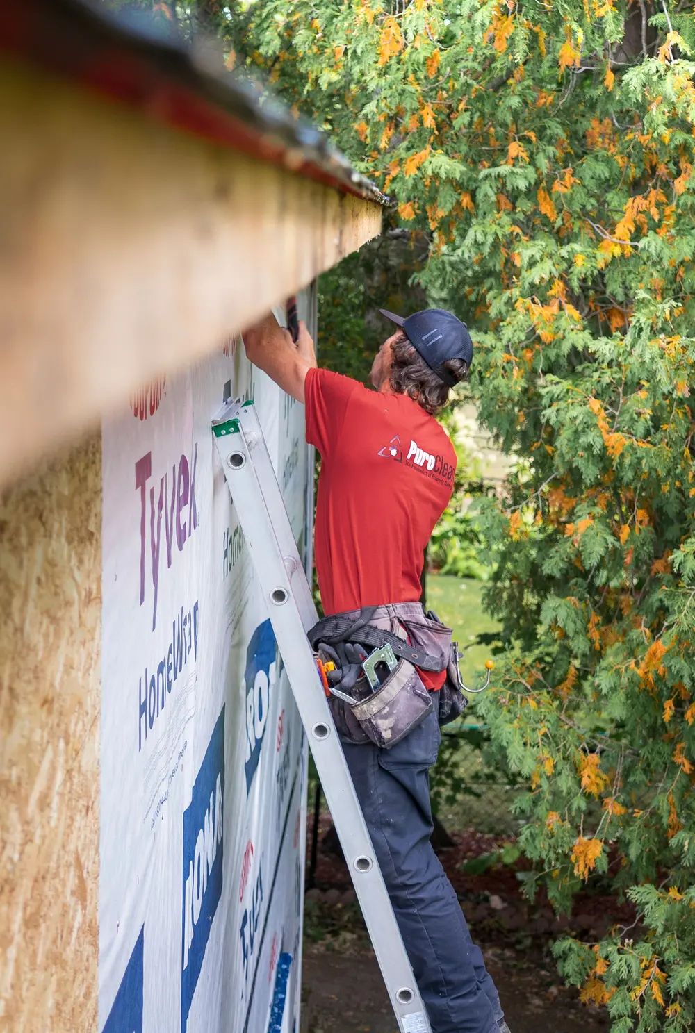 Repair worker on a ladder at a house wall stripped to its weather wrap