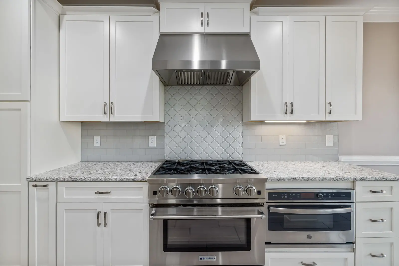 White kitchen with a stainless range hood installed over the stove