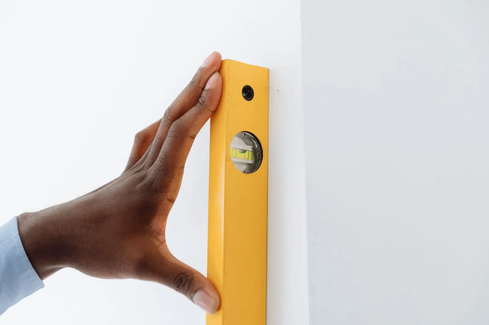 Hand holding a yellow level against a white wall to check a repair