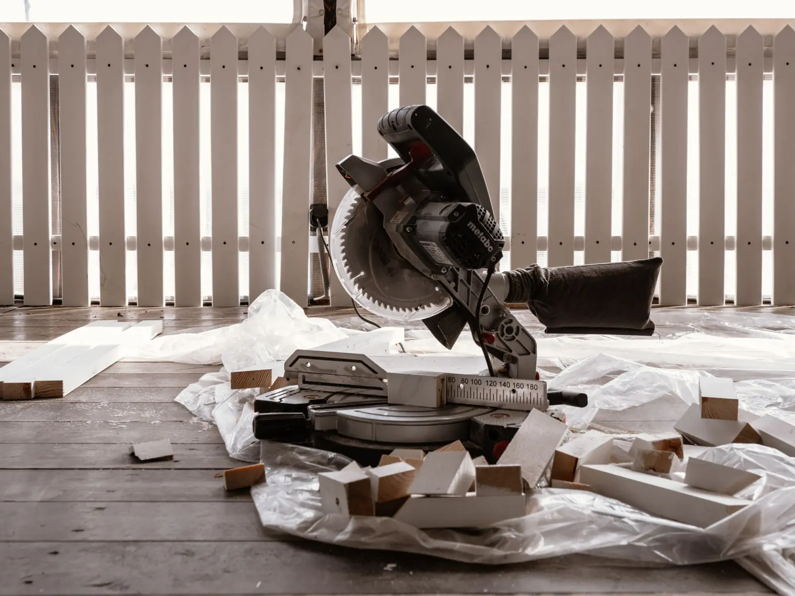 Miter saw set up on a deck beside a white picket fence during a repair