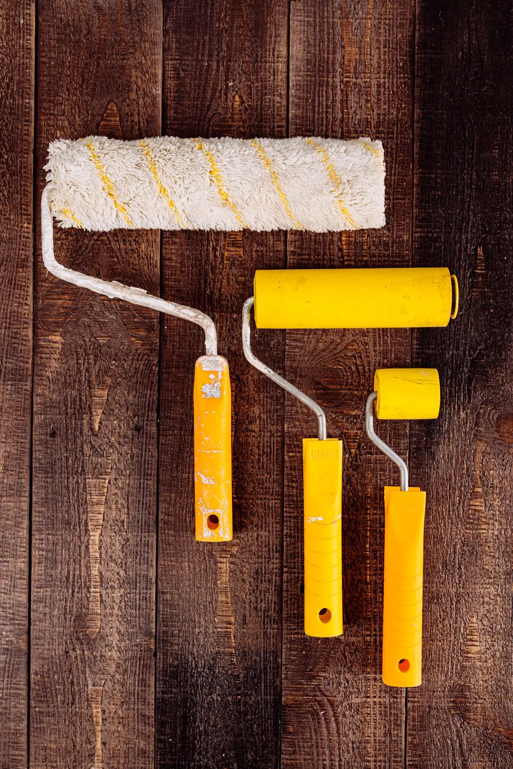 Paint rollers in three sizes laid on dark walnut boards